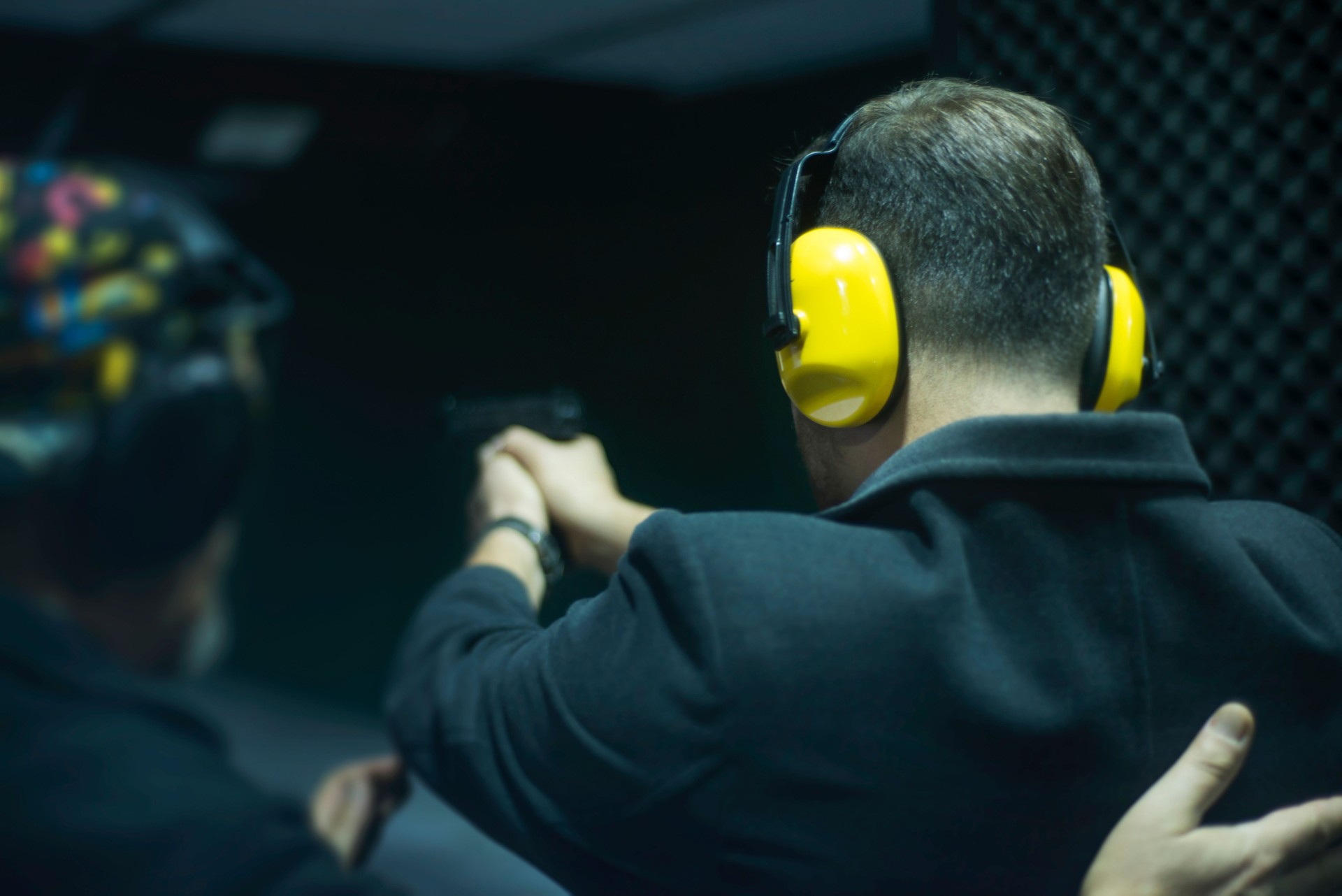 Unrecognizable instructor teaching how to shoot, giving briefing to young man at the shooting range